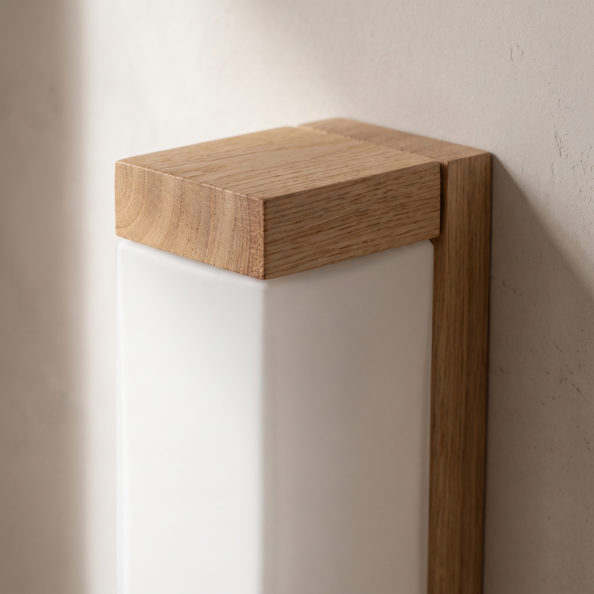 Close-up of the solid oak top cap and frosted glass column joinery on the wood wall sconce